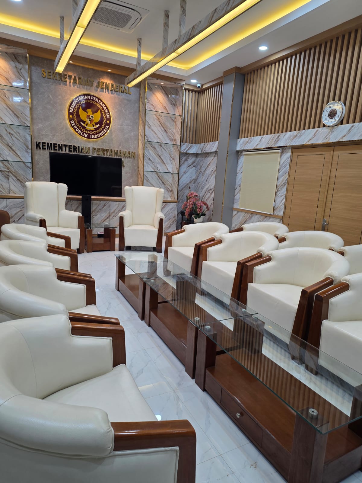 Interior ruang tamu kantor dengan kursi putih, meja kaca, dan panel dinding marmer
