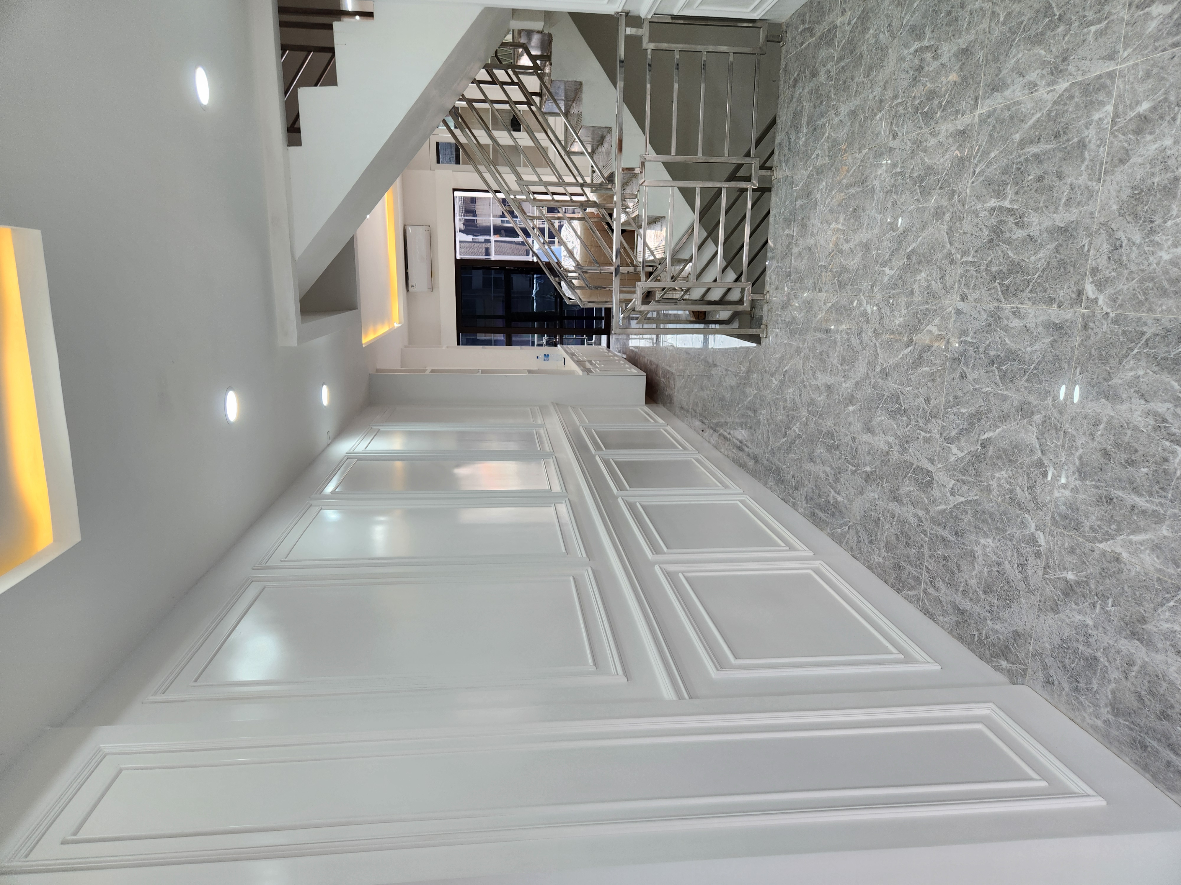 Interior rumah dengan wall moulding putih, lantai marmer, dan tangga